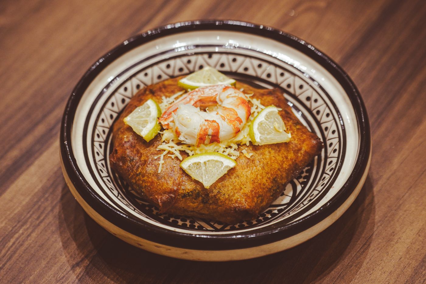 Scrumptious Moroccan seafood bastilla garnished with prawns and lemon slices served in a traditional dish.