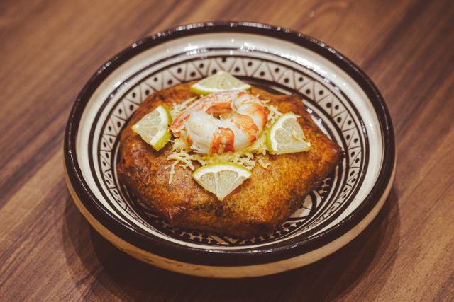 Scrumptious Moroccan seafood bastilla garnished with prawns and lemon slices served in a traditional dish.