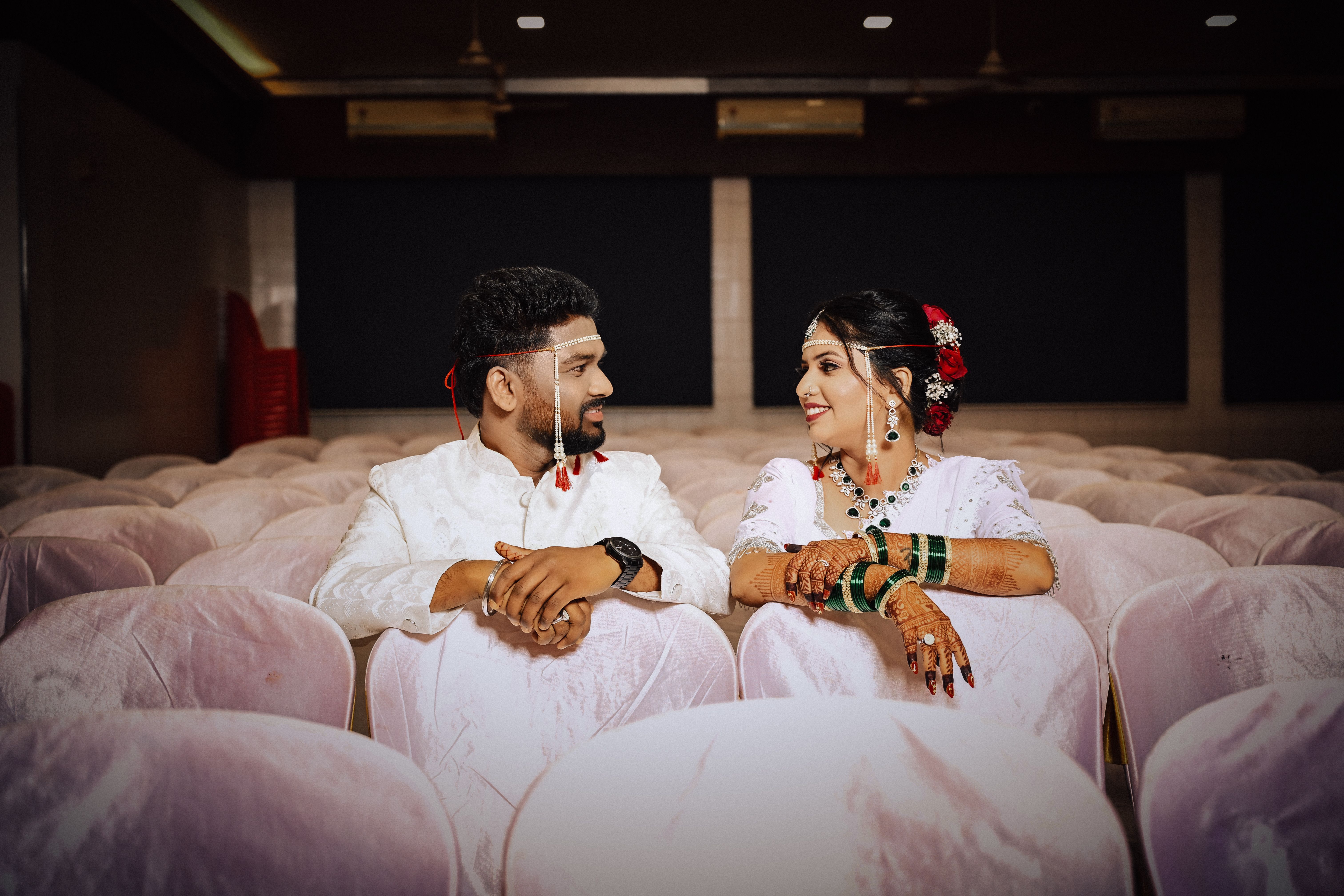 Smiling couple in traditional wedding attire sharing a moment in a plush indoor setting.