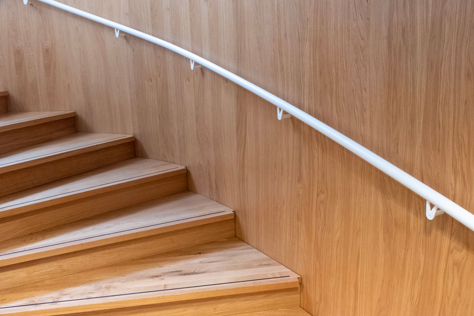 Minimalist wooden staircase with warm wood steps and a white handrail in an elegant home.