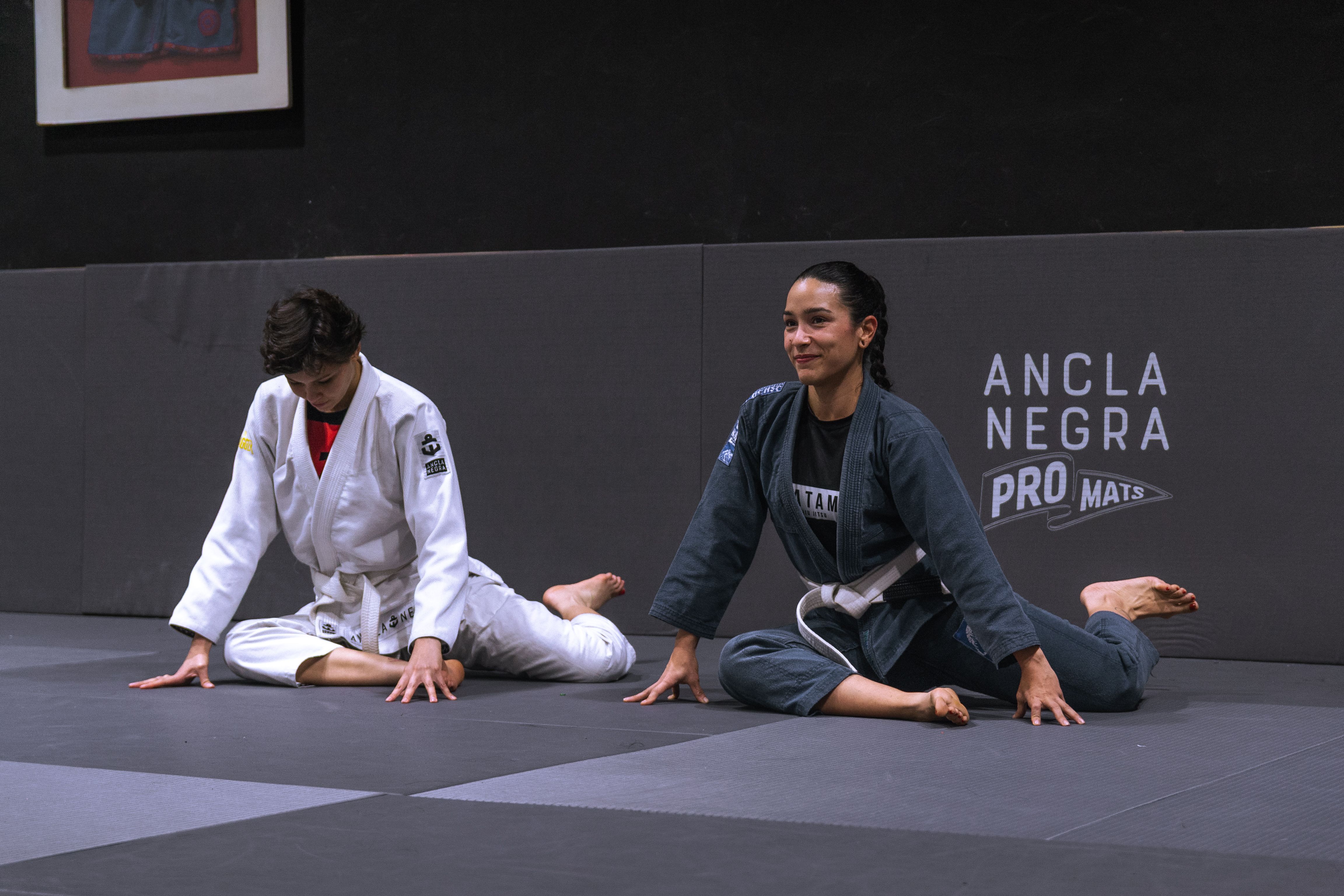 Two adults practicing jiu jitsu stretches in a training dojo, enhancing flexibility.
