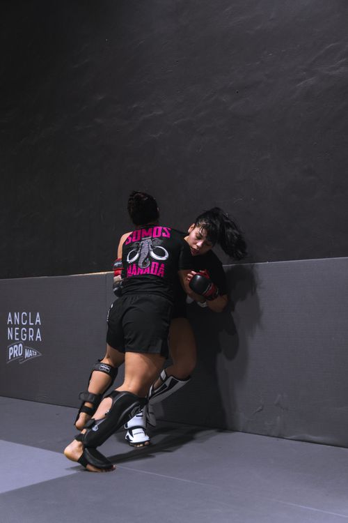 Free Two female fighters engaged in a fierce MMA training session against a padded wall indoors. Stock Photo