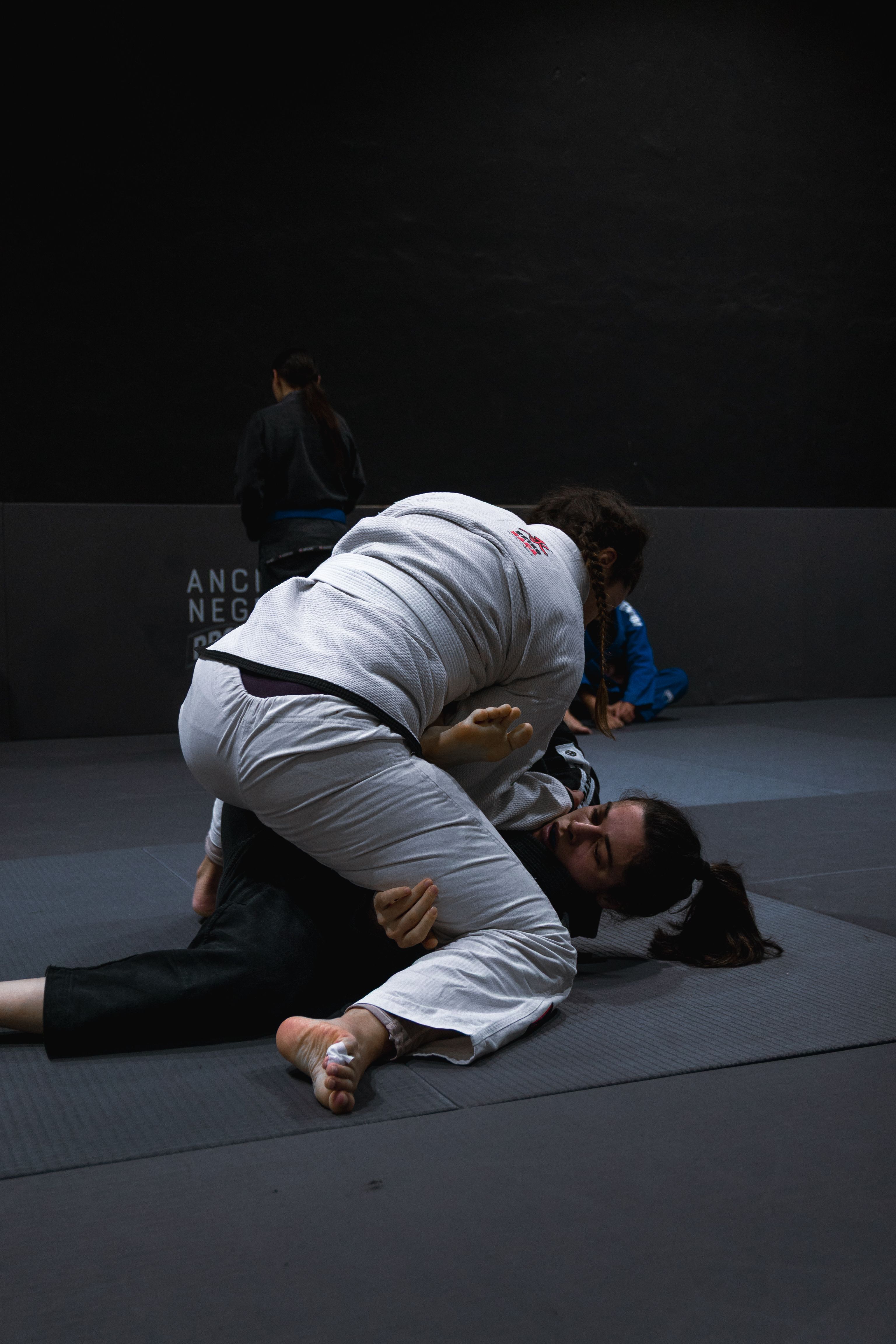 Two adults practicing Brazilian Jiu-Jitsu sparring session indoors.