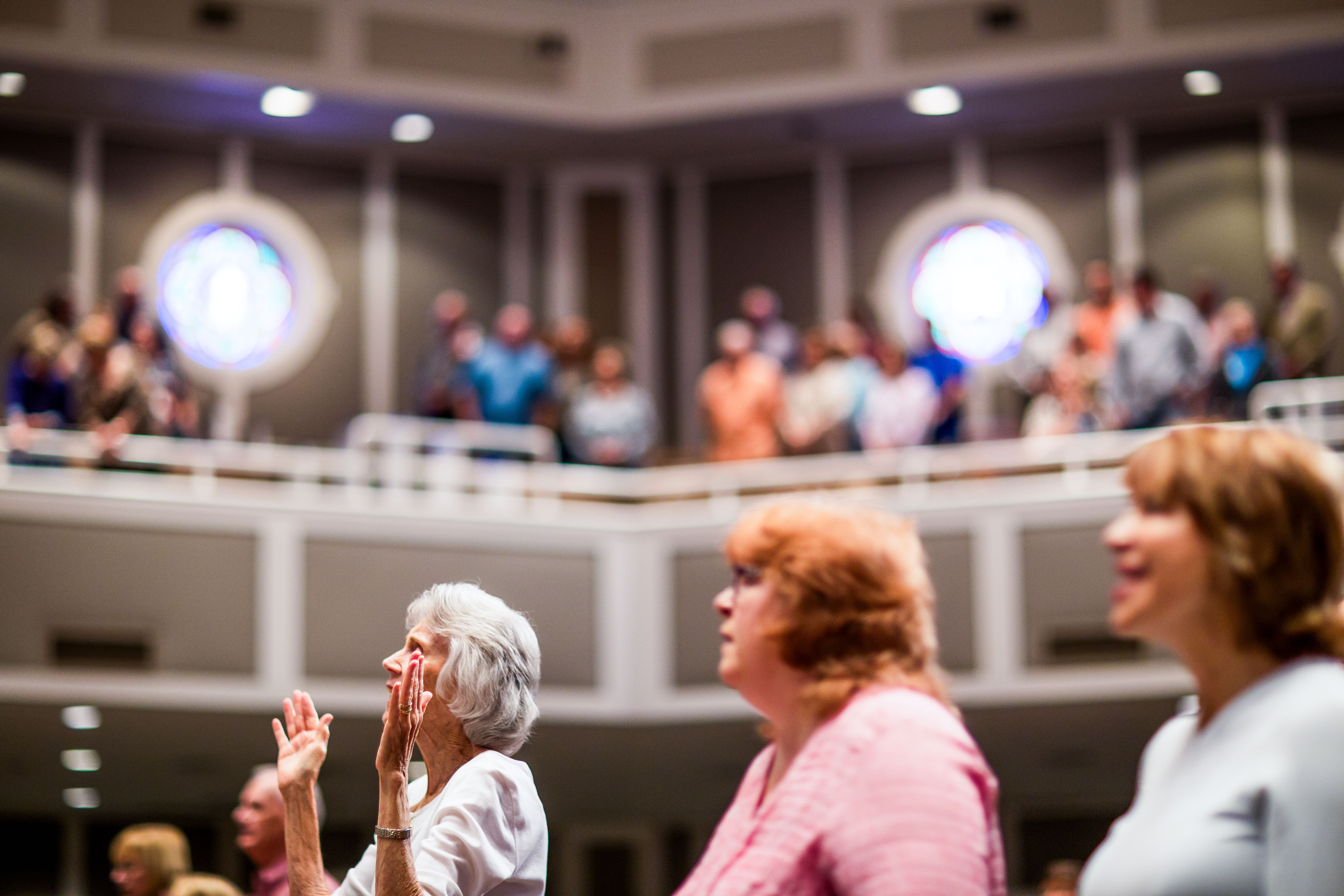 Senior woman engaging in worship during an indoor church service, with a congregation in the background.