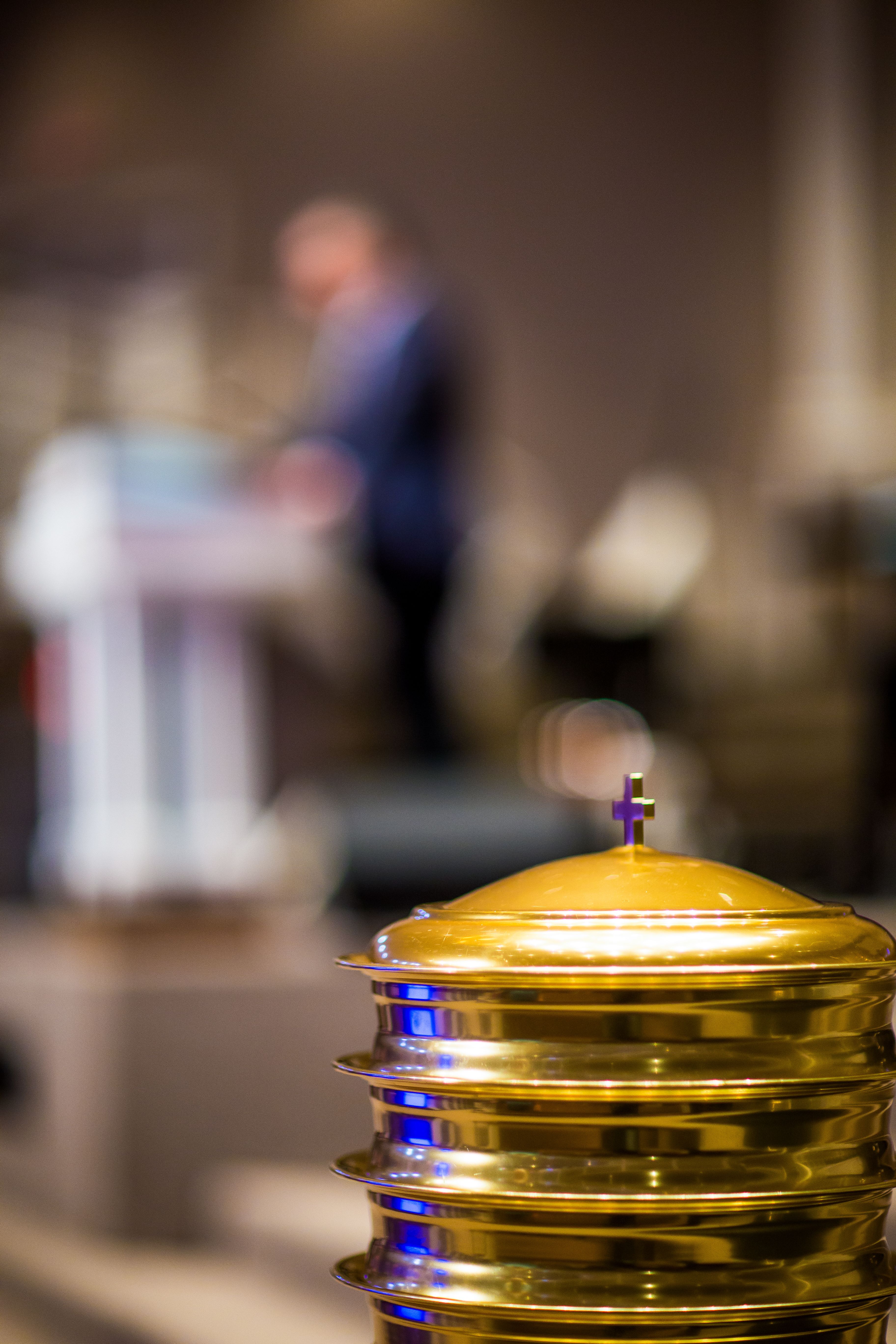 Gold communion tray with blurred congregation and pastor background, in a church setting.