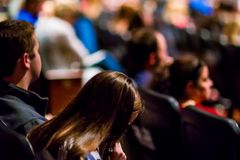 A focused shot of a person reading amidst a large audience in an indoor auditorium.
