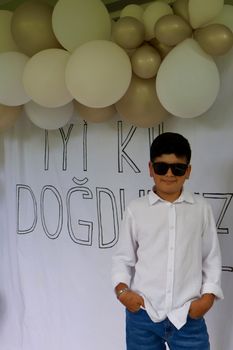 Young boy in sunglasses posing at a birthday party with balloons.