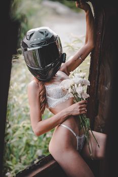 A woman in lingerie and motorcycle helmet poses creatively, blending fashion and adventure.