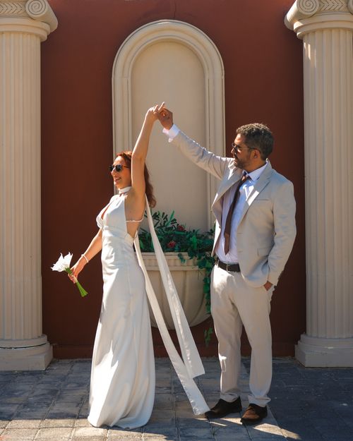 Free A joyful couple dances outdoors during their wedding ceremony, surrounded by classical columns. Stock Photo