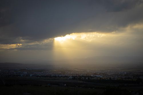Free Sunlight breaks through dark clouds over a city at sunset, creating a dramatic scene. Stock Photo