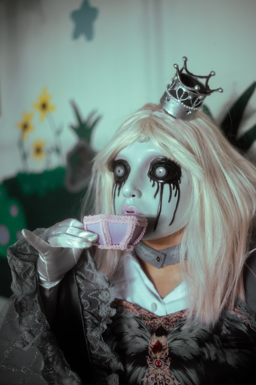 Free Eerie portrait of a doll-like figure with a porcelain mask and Victorian dress, sipping tea, in a surreal setting. Stock Photo