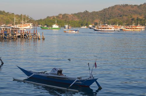 Free A traditional boat anchored in a scenic harbor with several vessels and lush hills in the background. Stock Photo