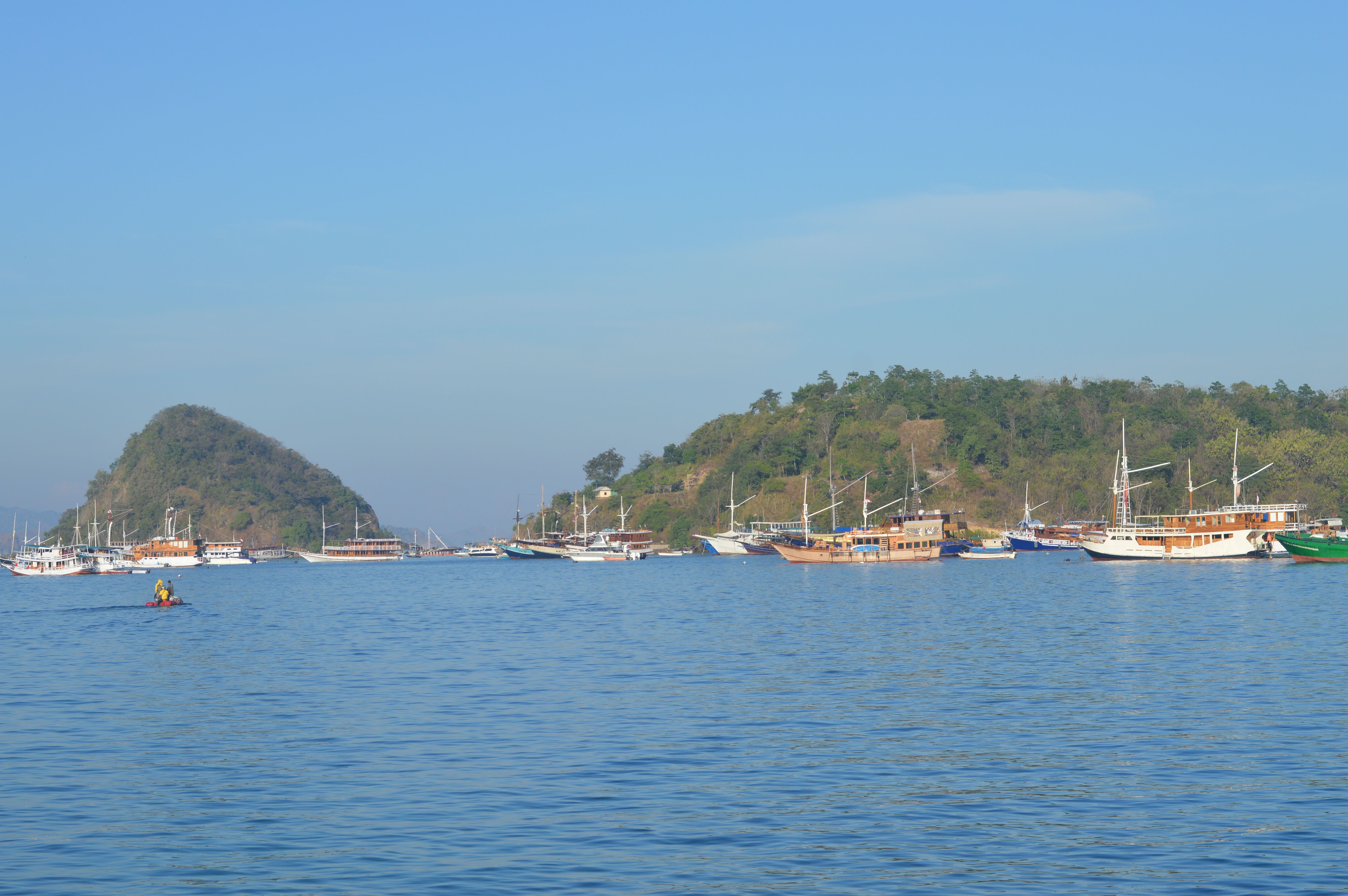 Idyllic scene of boats anchored near lush islands in Indonesia under a clear blue sky.