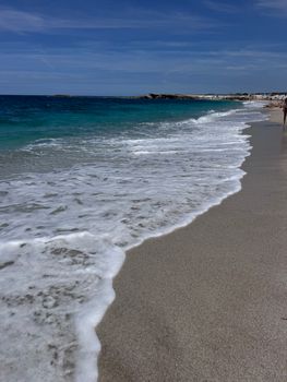 Experience the tranquil beauty of a sunny beach in Sardinia with gentle waves lapping against the shore.