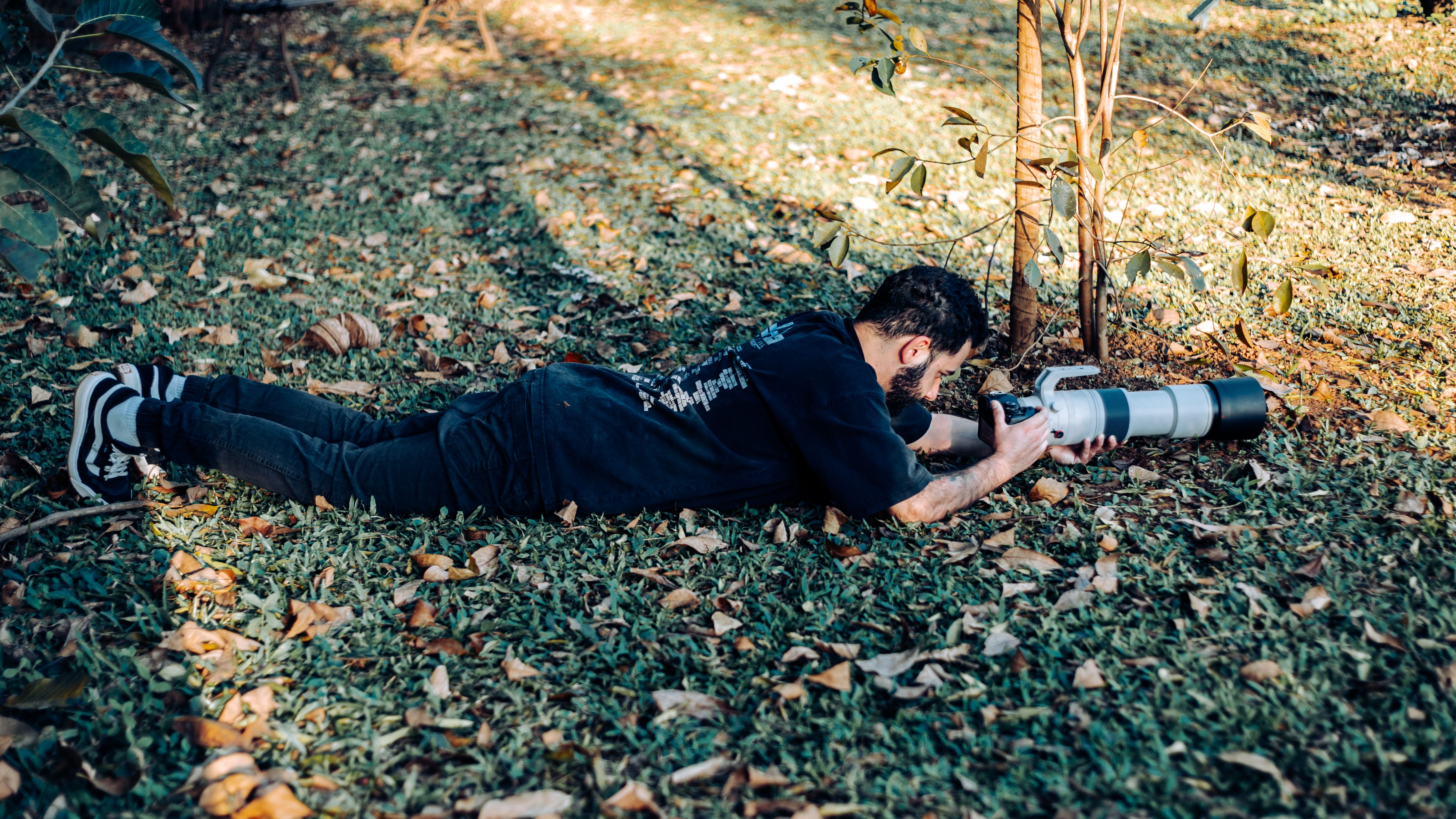 Man lying on grass photographing with telephoto lens outdoors in autumn.