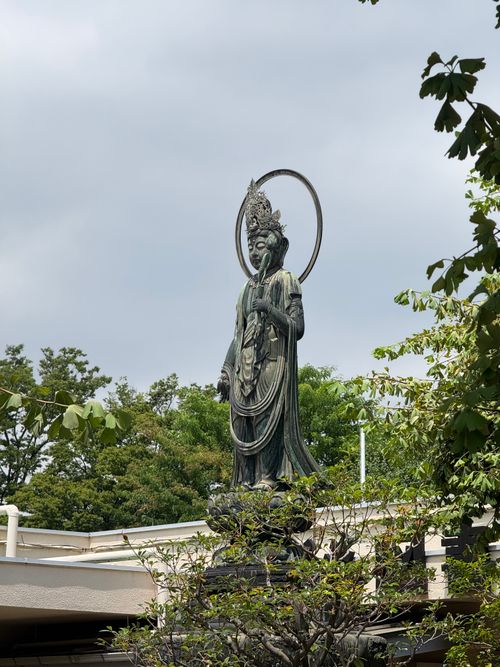 Free Serene Buddha statue surrounded by lush greenery in a Tokyo Temple garden. Stock Photo