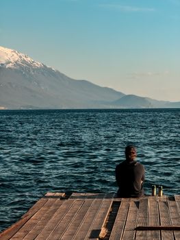 一个人在奥赫里德湖的码头上享受着宁静的时光，远处是连绵的群山。 - 相关推荐