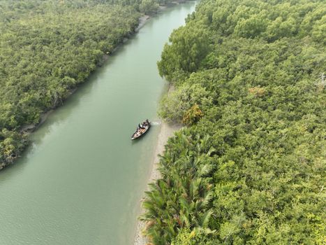 Aerial view of a small boat navigating the lush Sundarbans mangrove forest waterways.
