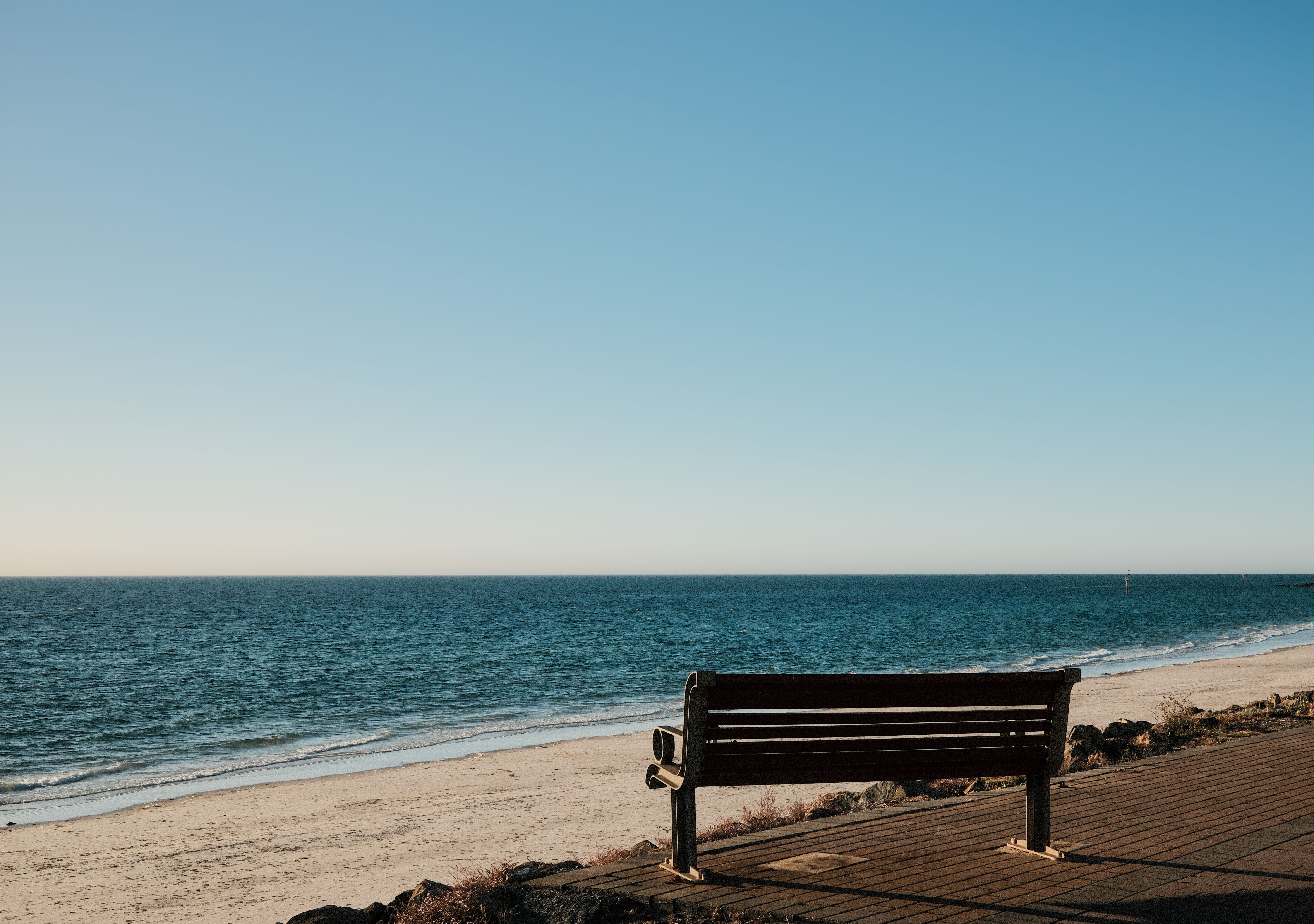 Serene view of an empty bench facing a tranquil ocean under a clear blue sky.