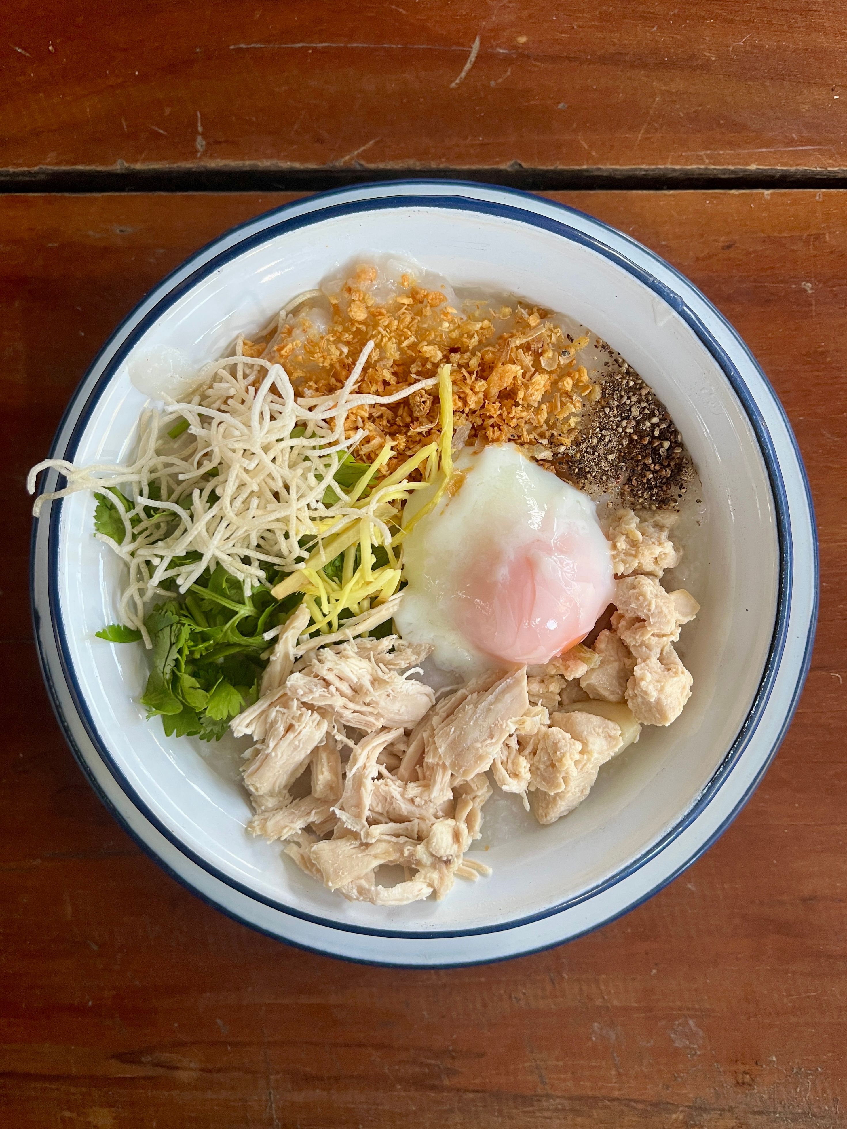 Top view of Thai chicken congee garnished with fresh herbs and a soft-boiled egg.