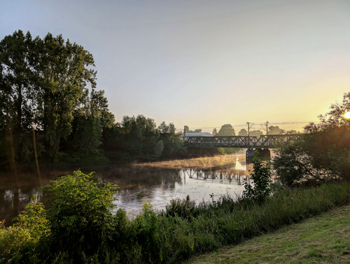 Free Serene river landscape at sunrise with a bridge and misty water reflections. Stock Photo