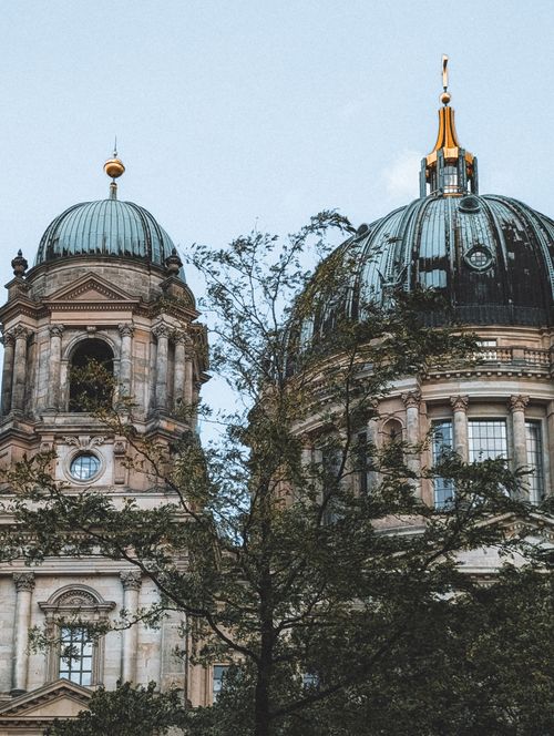 Free View of the ornate domes of Berlin Cathedral with tree foreground, showcasing architectural grandeur. Stock Photo