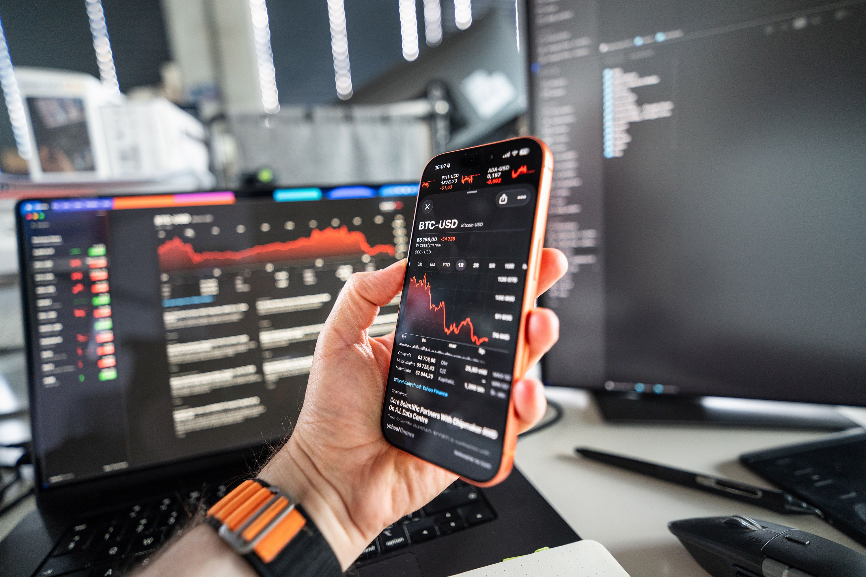 A person analyzing cryptocurrency trends on a smartphone with a declining chart on screen, set against a tech office background.