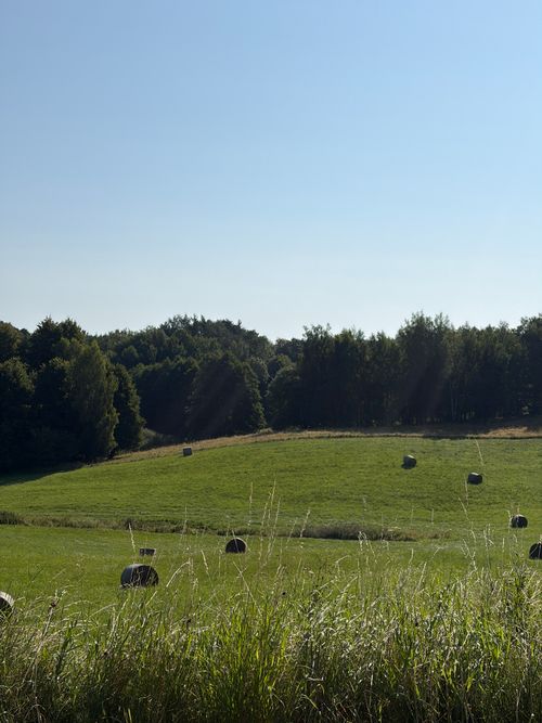 Free Serene rural landscape in Poland featuring hay bales on a green field under clear blue skies. Stock Photo