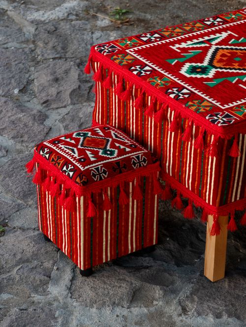 Free Vibrant handcrafted ottoman and table featuring traditional red and white textile designs with tassels, set on a rustic stone floor. Stock Photo