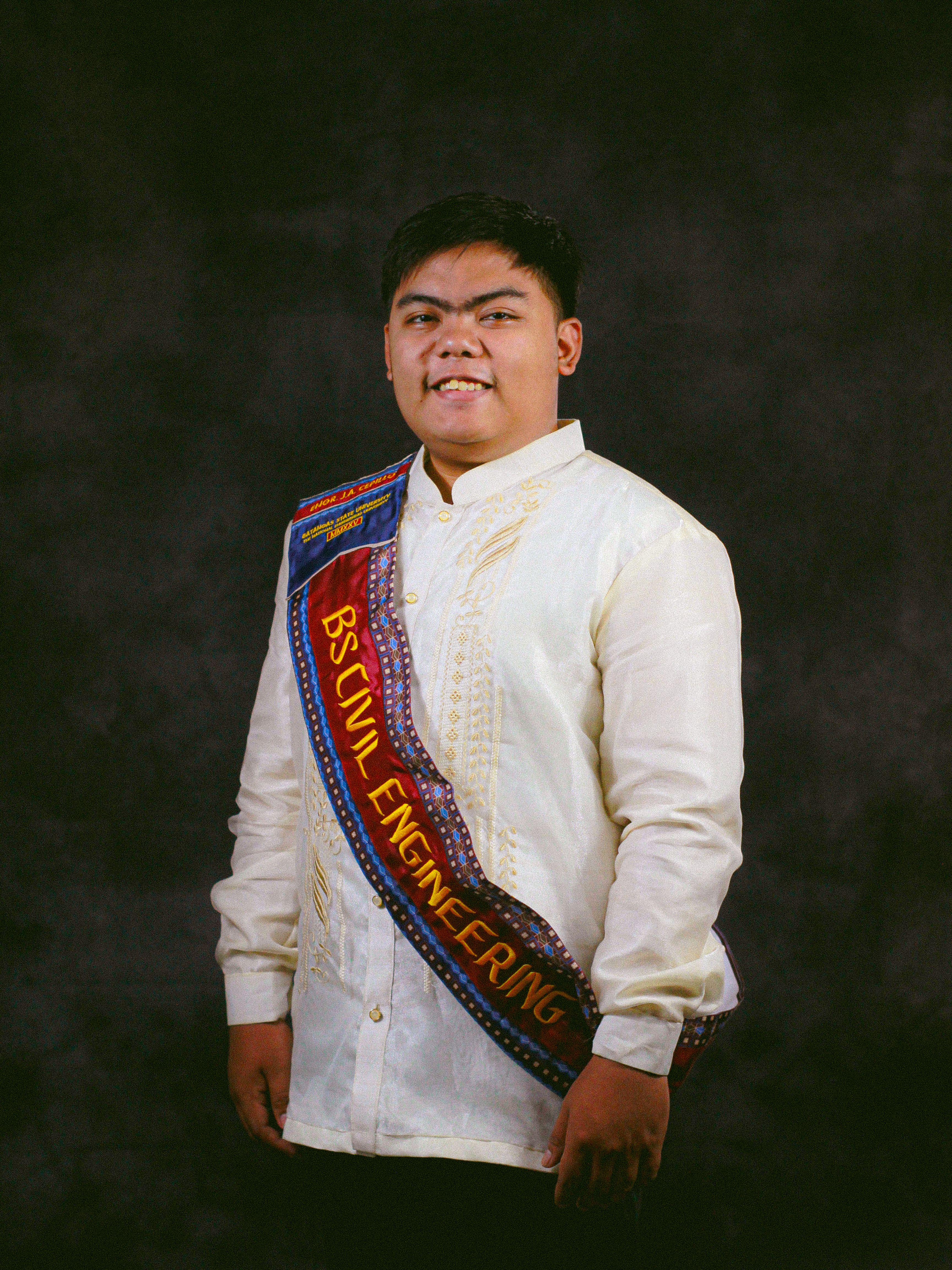 Proud civil engineering graduate posing in traditional attire with a sash.