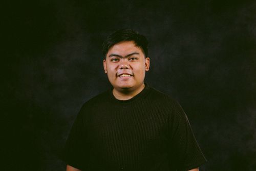 Free Smiling man in a textured black shirt against a dark backdrop, studio portrait. Stock Photo
