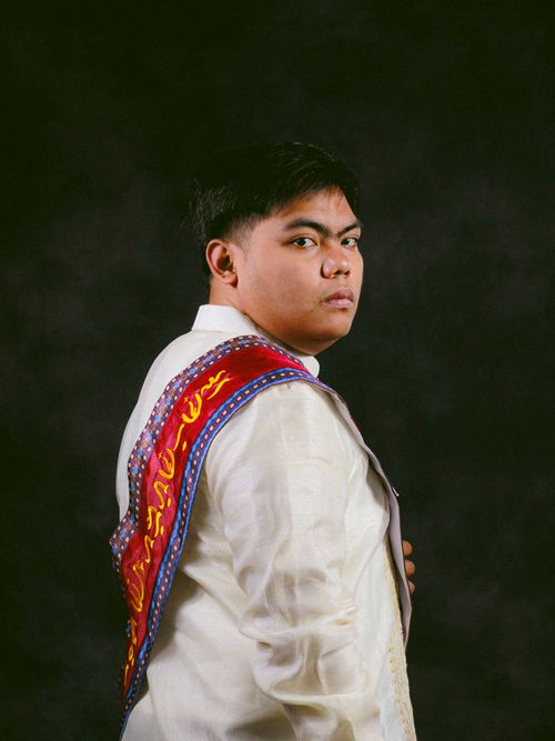 Free Portrait of a man wearing a traditional barong with a vibrant sash, set against a dark background. Stock Photo