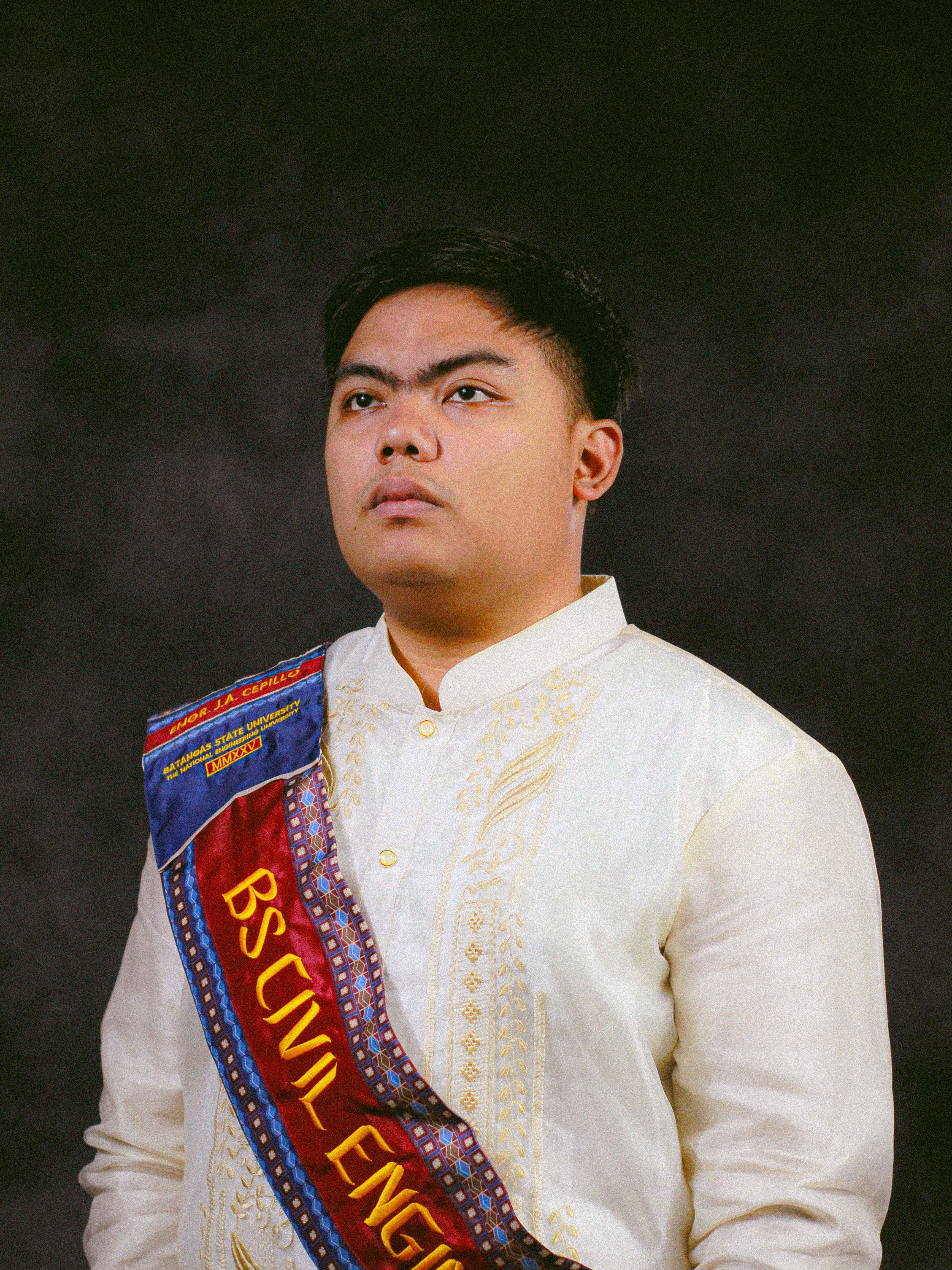 Studio portrait of a young graduate in traditional attire with a Civil Engineering sash.
