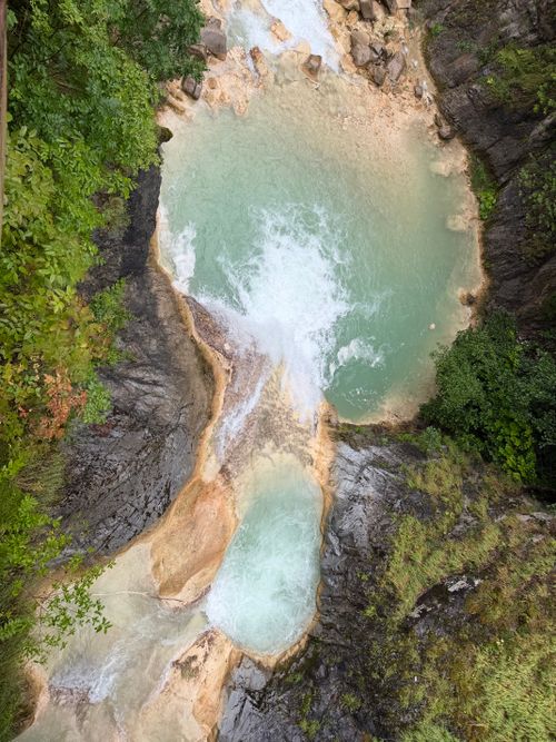 Free Stunning aerial shot of a cascading waterfall flowing through rocky terrain surrounded by lush greenery. Stock Photo