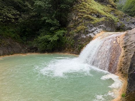 A tranquil waterfall cascades into a turquoise pool amidst lush greenery, capturing a serene natural setting.