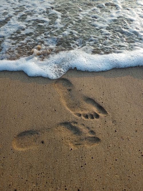 Free Footprints in the sand with waves washing ashore, capturing a serene coastal moment. Stock Photo
