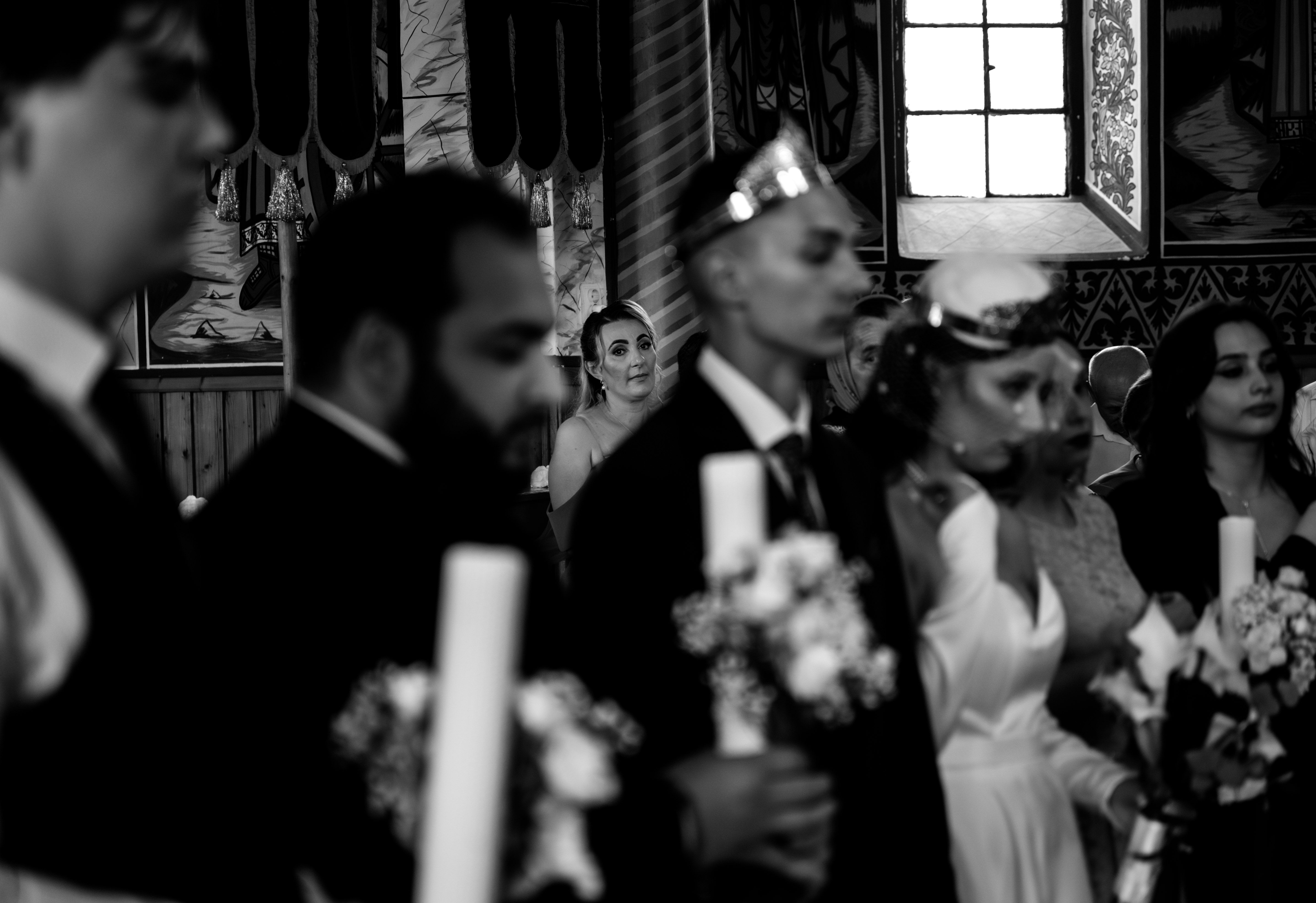 A black and white photograph capturing a Romanian wedding ceremony inside a church.