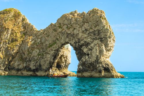 Free A vivid coastal scene featuring the iconic Durdle Door rock arch with a boat on crystal clear waters. Stock Photo