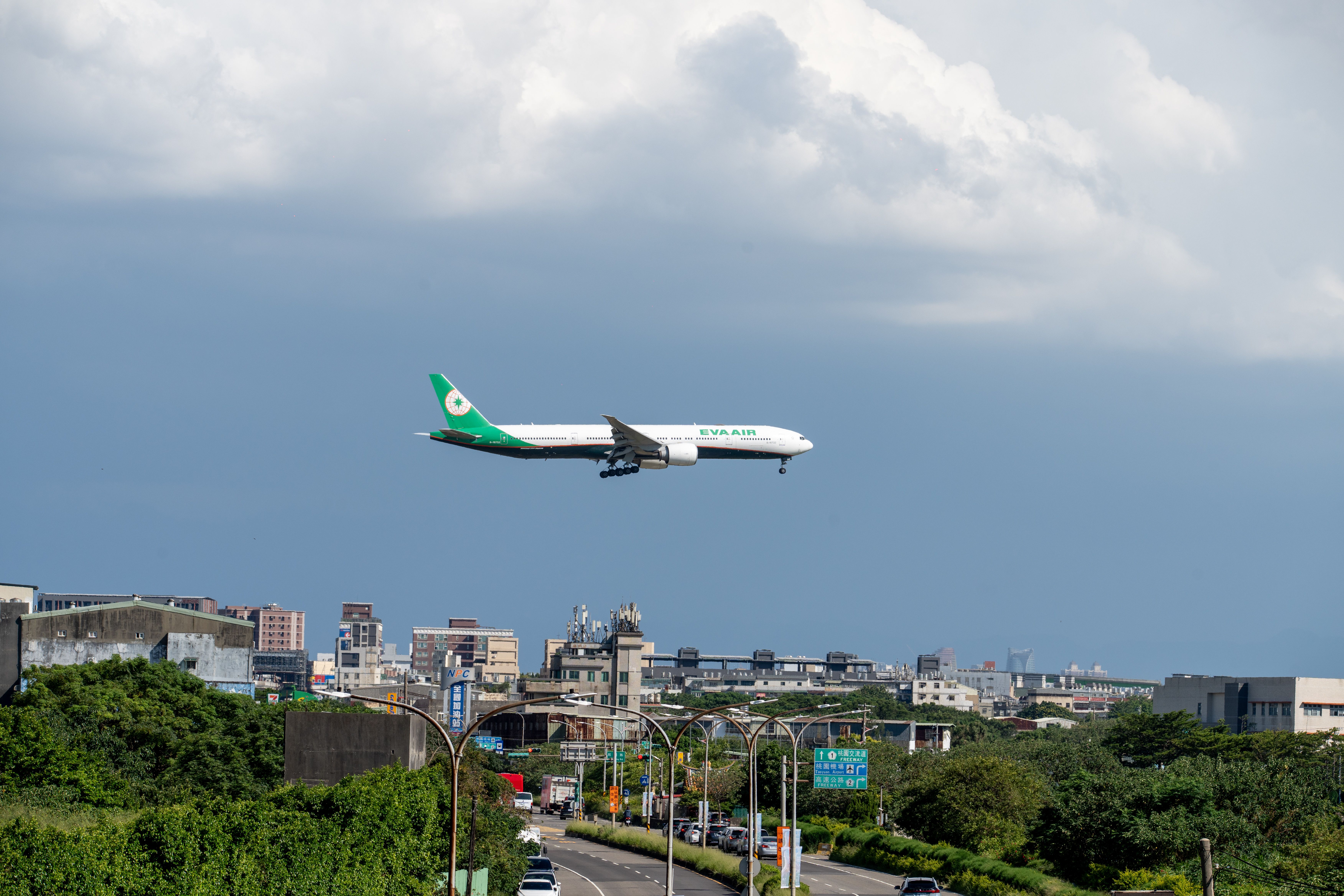 Airplane descends over urban landscape on a clear day with scattered clouds.