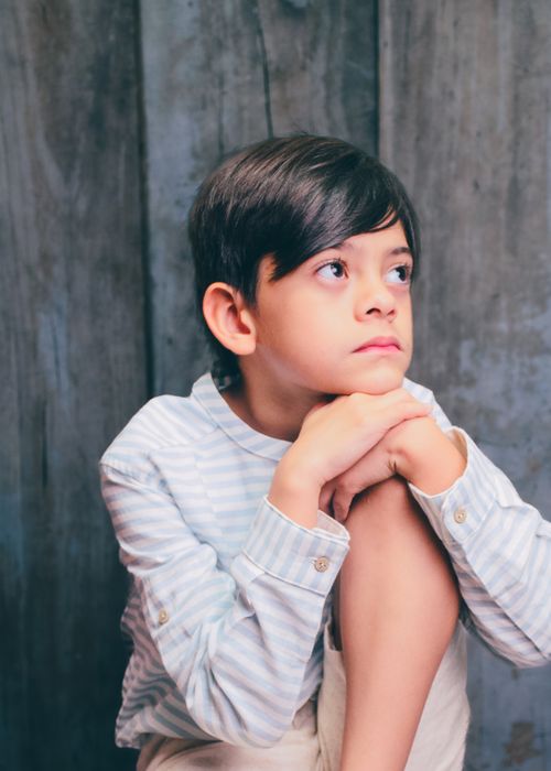 Free A pensive child looks upwards against a wooden backdrop indoors. Stock Photo