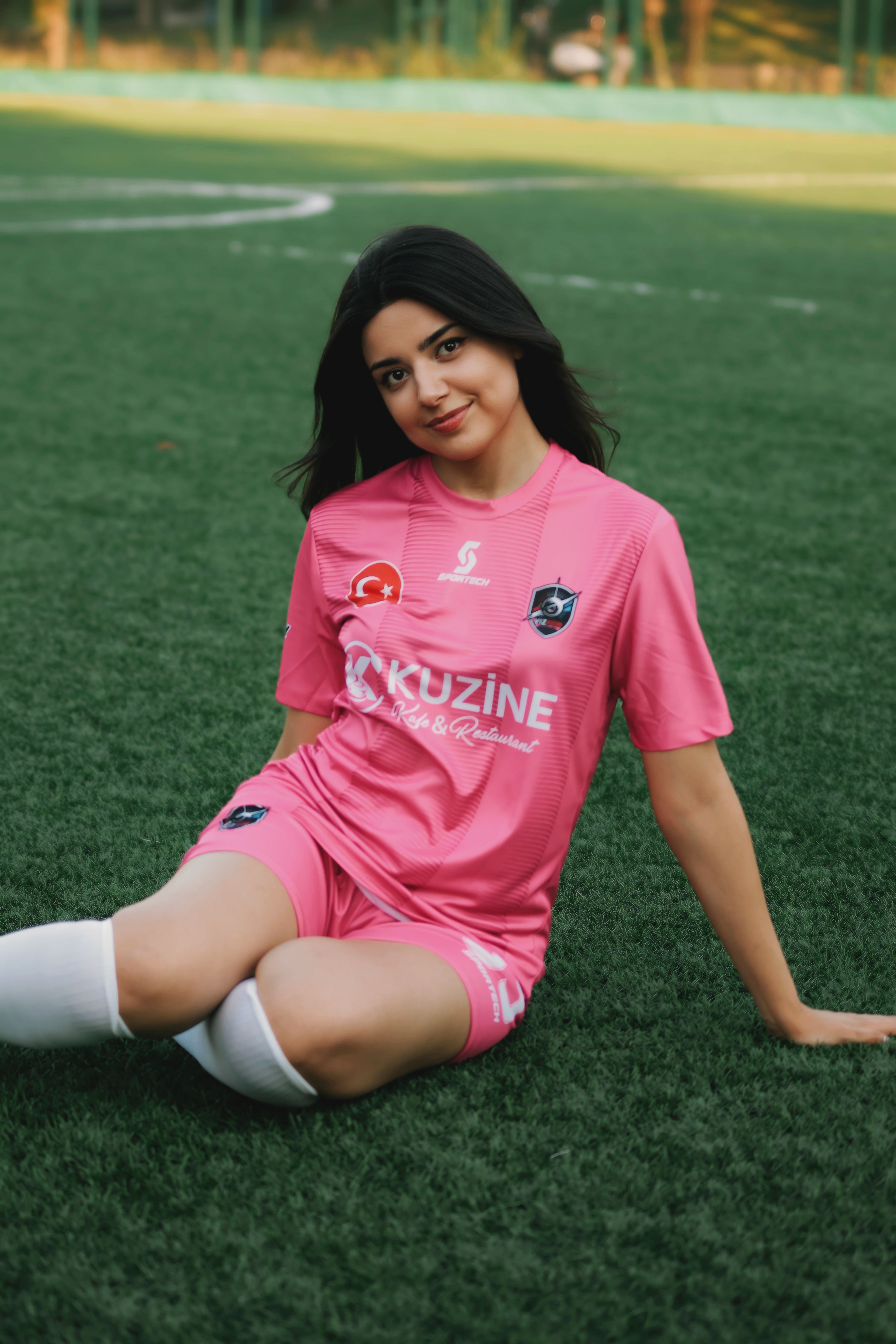 Young woman soccer player in pink uniform sitting on grassy field.
