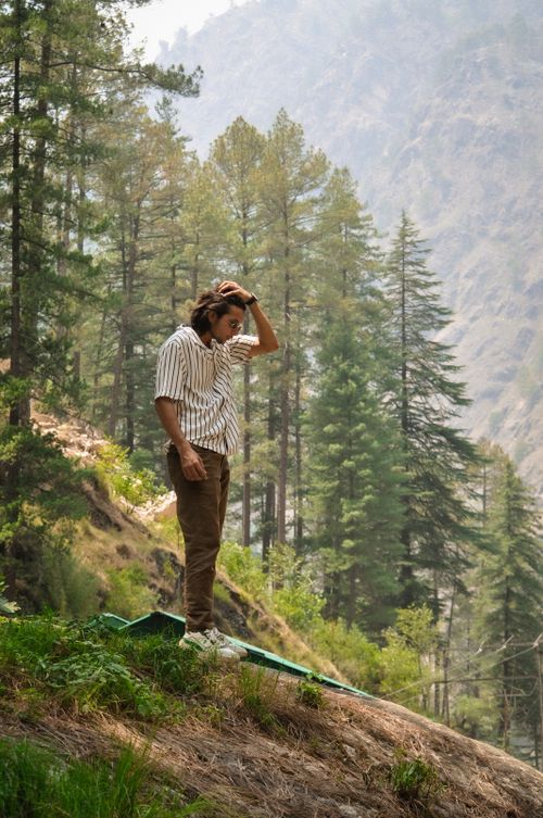 Free A young man stands in a serene forest clearing in India, surrounded by lush trees and misty mountains. Stock Photo
