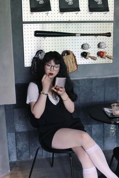 Stylish woman applying lipstick in a cafe setting, capturing modern lifestyle and beauty.