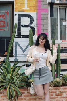 Smiling woman with drink poses stylishly against a vibrant wall mural framed by tall cacti.