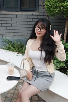 Smiling young woman in casual attire sitting outdoors with a drink and phone.