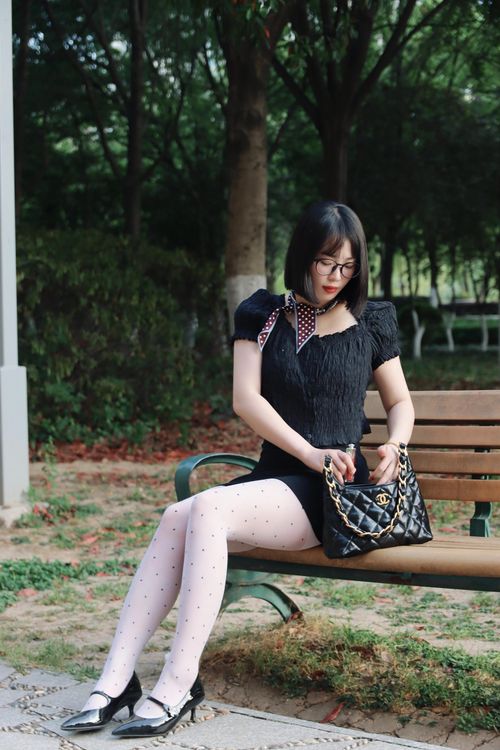 Free Woman in elegant black dress seated outdoors with a chic handbag on a park bench. Stock Photo