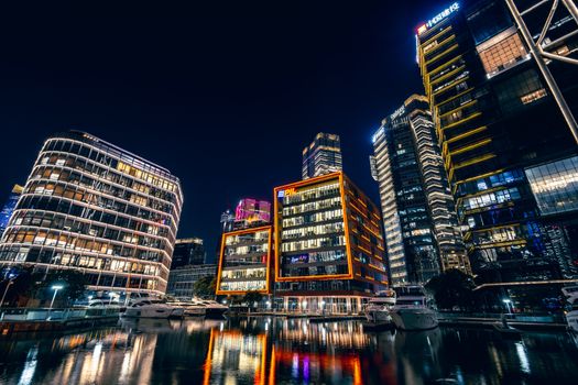 Vibrant city skyline at night with colorful illuminated skyscrapers reflecting on water.