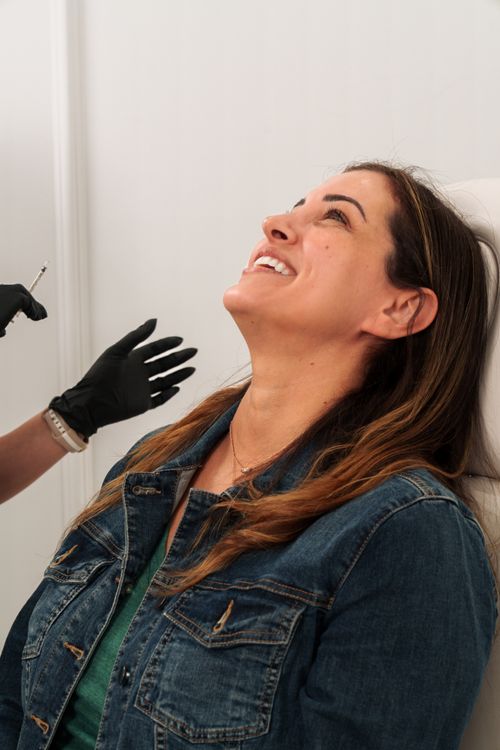 Free A woman in a denim jacket smiles as she receives a cosmetic injection in a med spa setting. Stock Photo