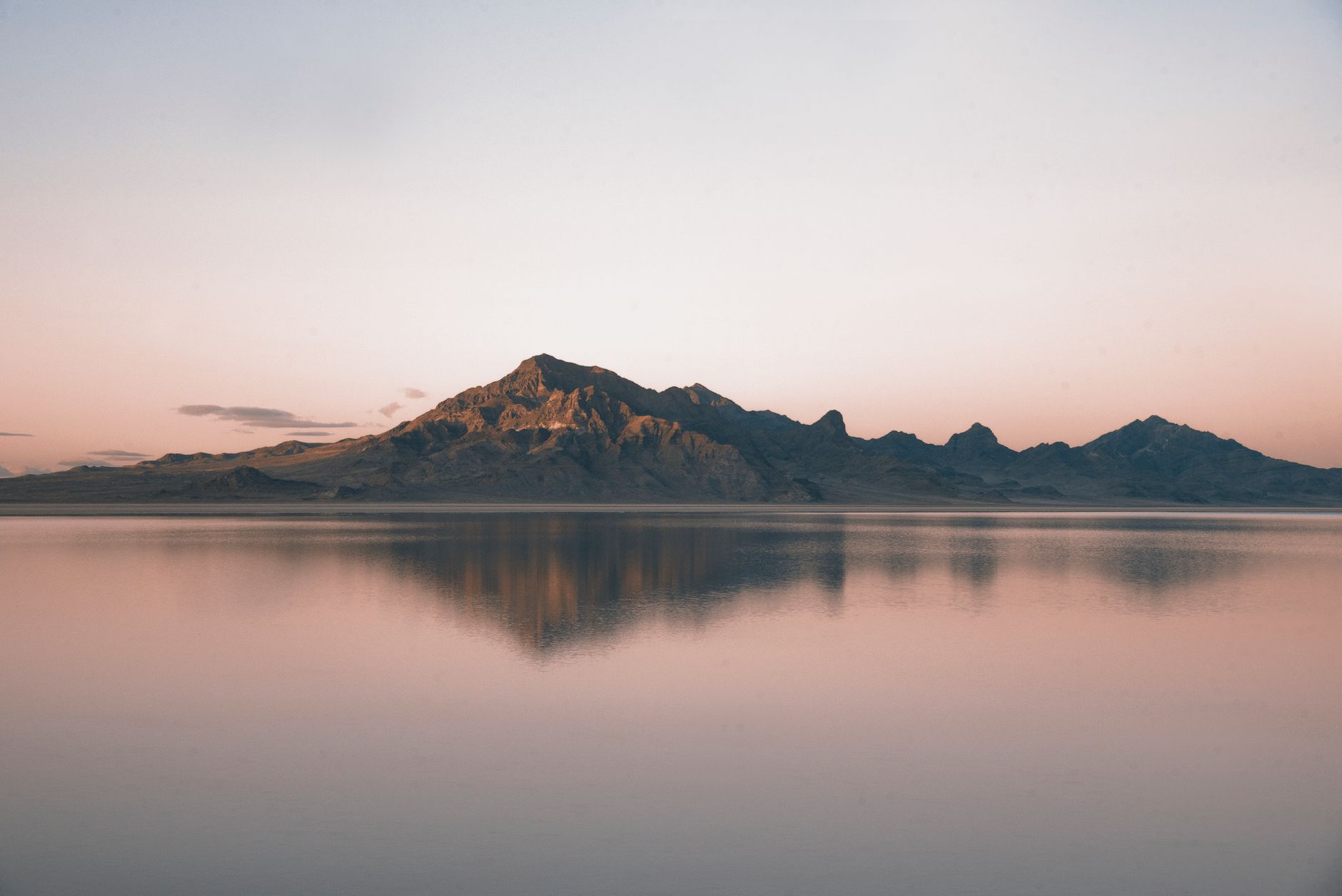 Tranquil mountain landscape with mirrored reflection in calm water at sunrise.