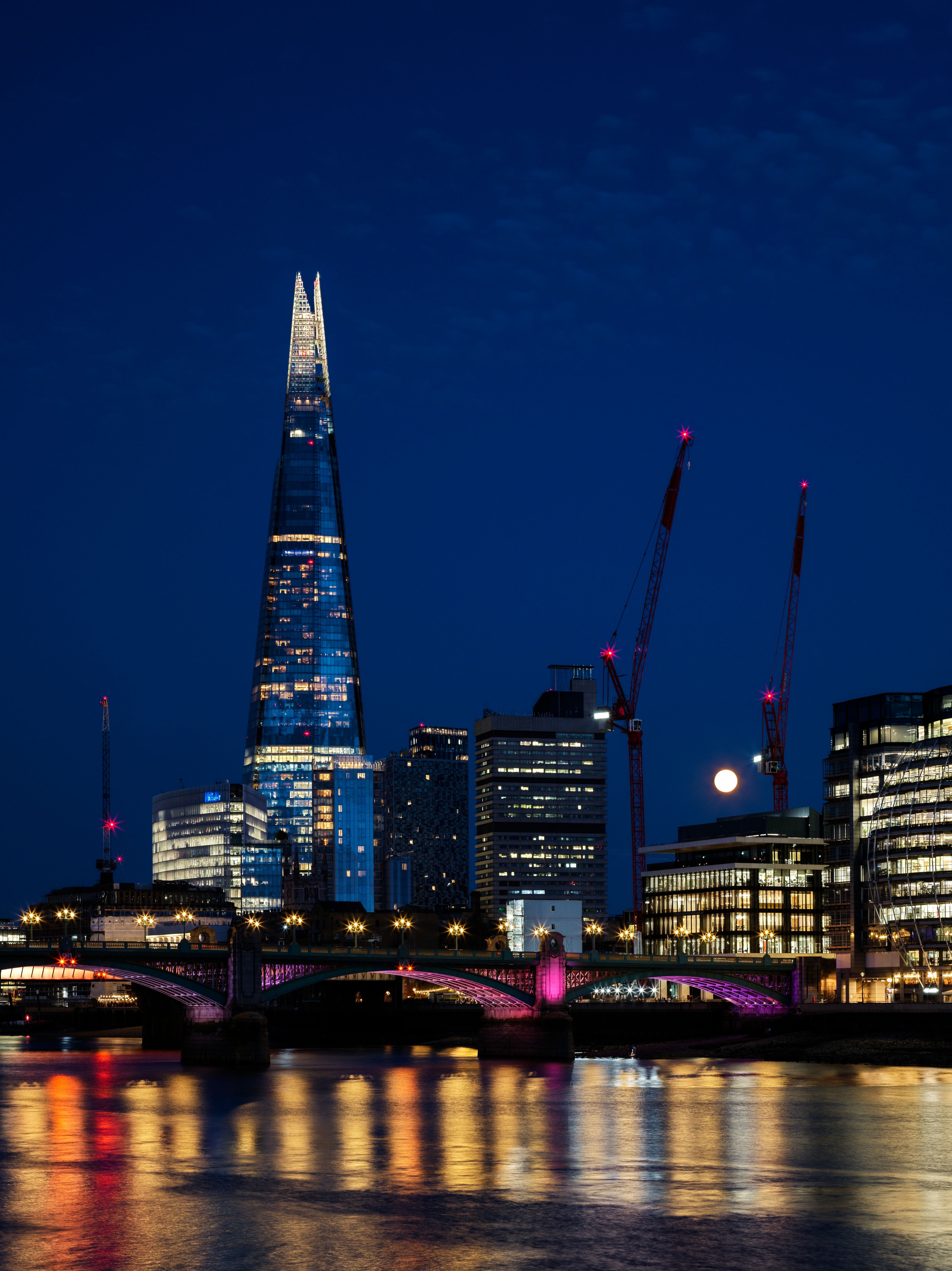 Stunning nighttime cityscape of The Shard and London skyline with reflections in the Thames.